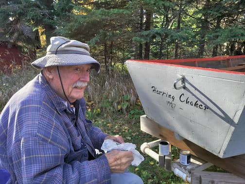 John Franz painting letters and images on a 94-year-old herring skiff which was renovated by Tor Torkildson.